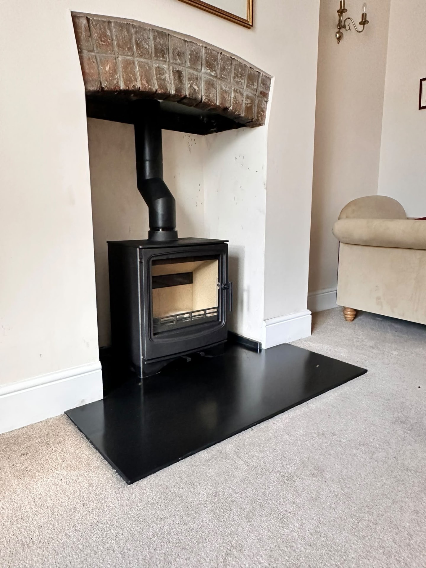 Black wood burner under a brick arch in a carpeted living room with cream walls