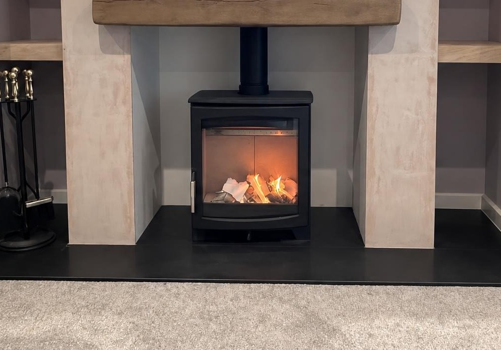 Lit wood burner in a media wall with alcove shelving and a rustic oak beam mantel