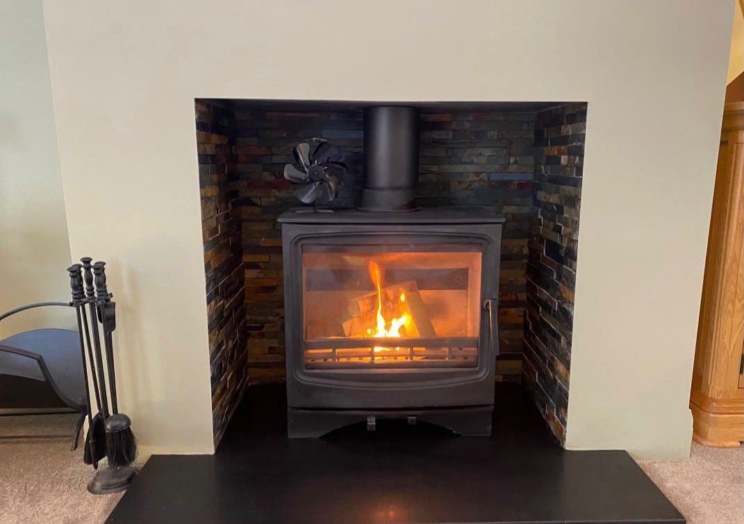A lit wood burner set in a split-face slate fireplace recess in a living room
