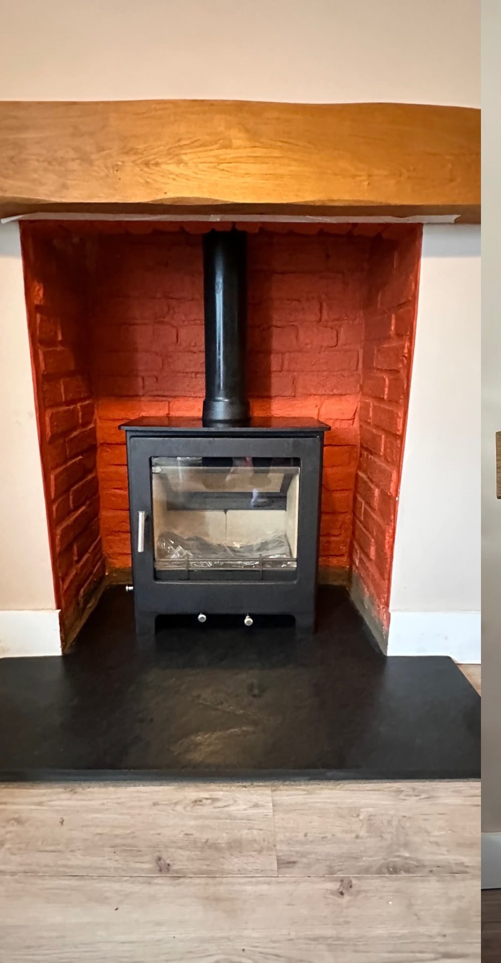 Black stove in a painted brick chamber with a wooden beam mantel and slate hearth