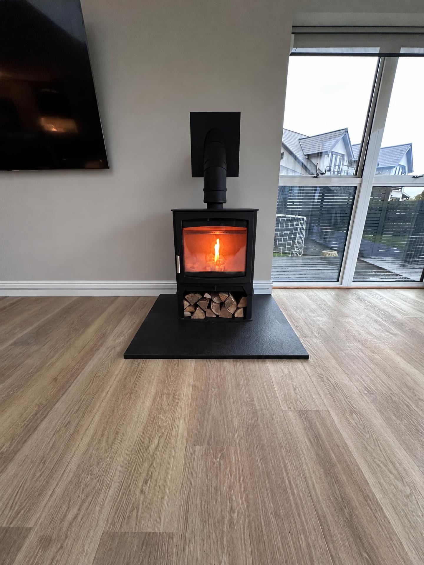 Lit wood burner on a log store in a modern living room with patio doors out to the garden