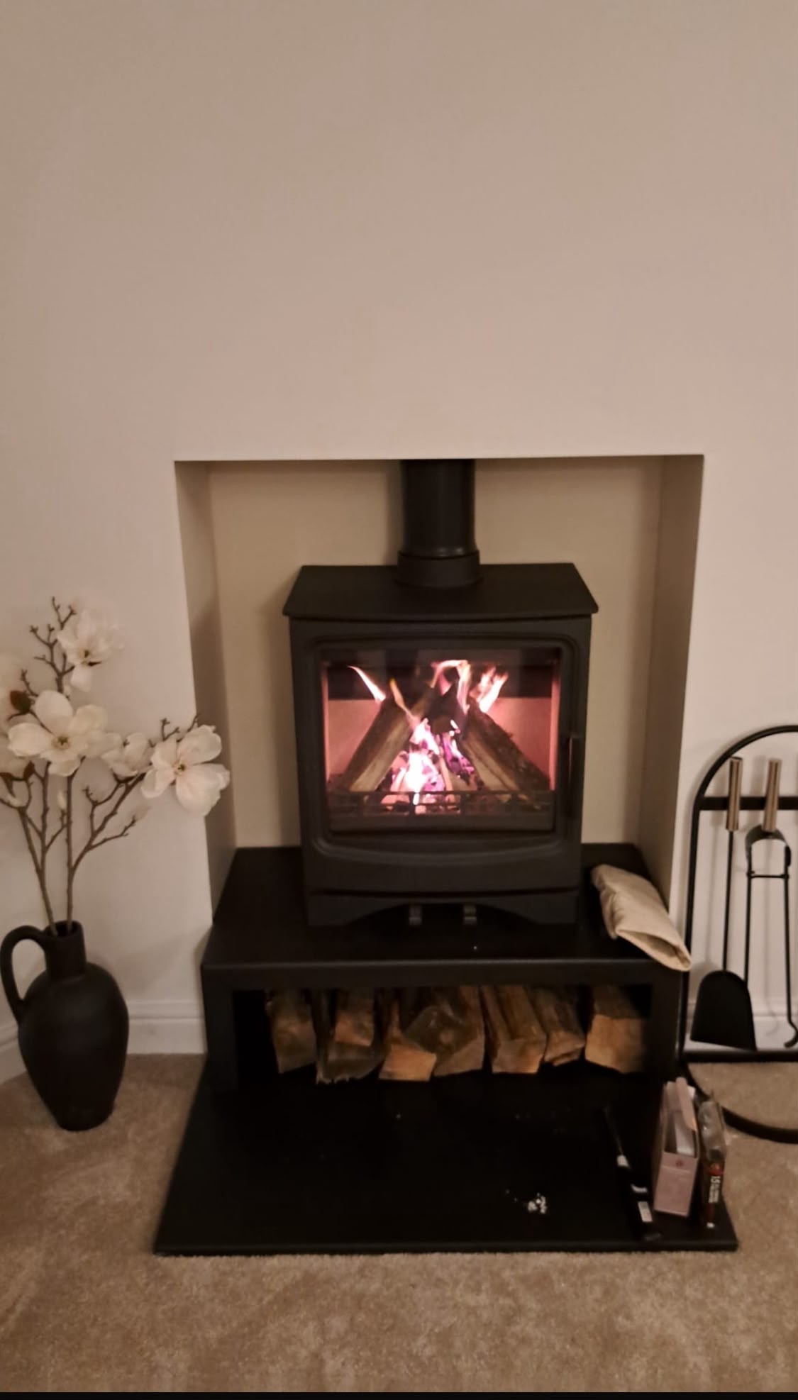 Lit wood burner on a matching log store stand in a carpeted living room