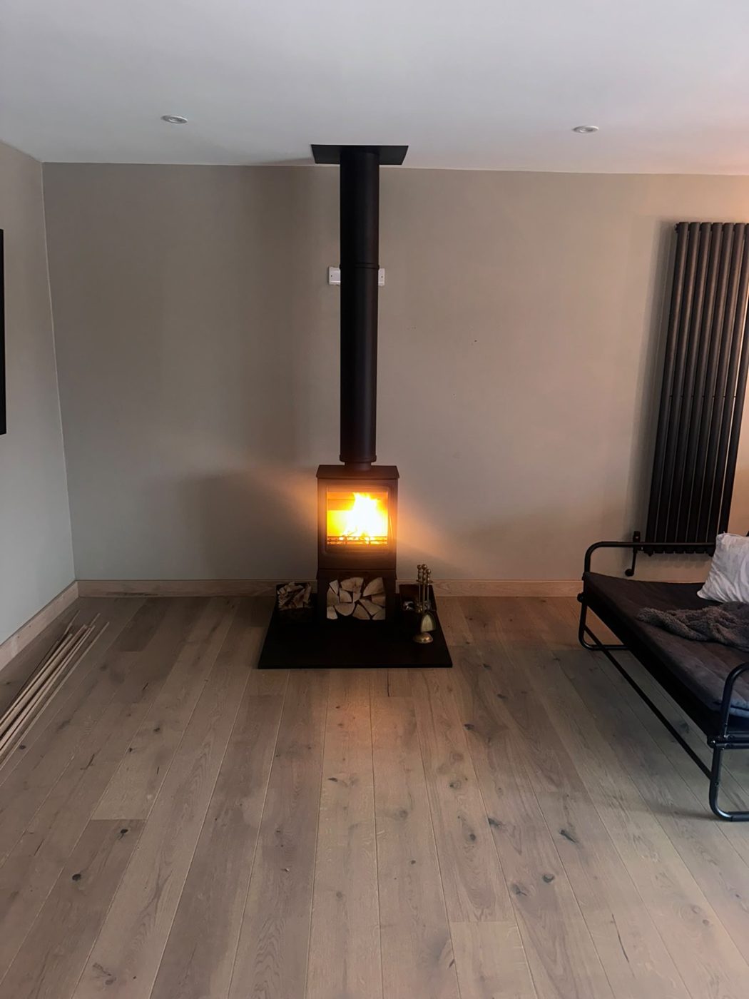 Freestanding stove with tall black flue lit in a modern living room